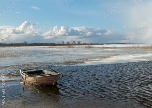 winter landscape with lake, old wooden boat in the lake, expressive clouds, Lake Burtnieki