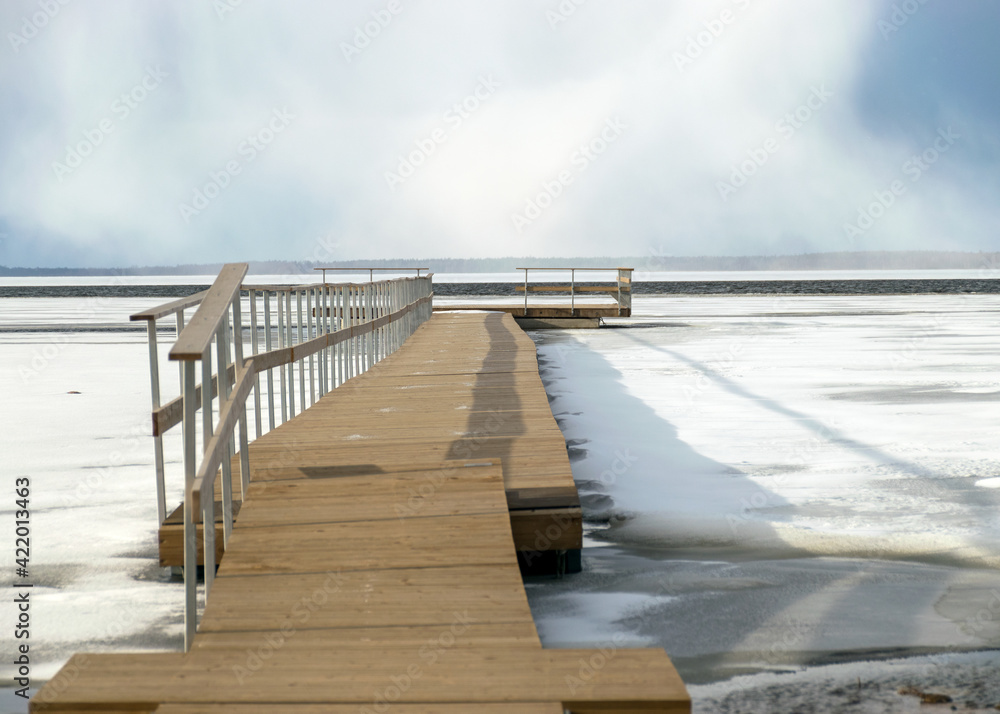 Obraz premium winter landscape on a wooden footbridge in the lake, the surface of the lake is partially covered by ice, cold winter day by the lake, Lake Burtnieki