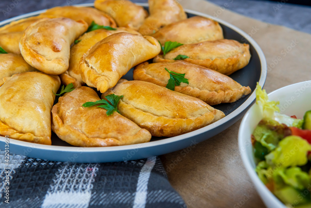 Traditional Latin American baked beef empanadas on a plate with a fresh salad sidedish. Gluten free savory pastries with meat beef stuffing or filing. Handmade Typical dish in Spain or Argentina. Traditional Latin American baked beef empanadas on a plate with a fresh salad sidedish. Gluten free savory pastries with meat beef stuffing or filing. Handmade Typical dish in Spain or Argentina.