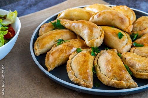 Traditional Latin American baked beef empanadas on a plate with a fresh salad sidedish. Gluten free savory pastries with meat beef stuffing or filing. Handmade Typical dish in Spain or Argentina.
