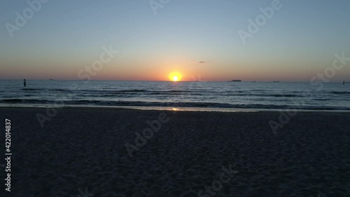 Drone flight over the beach and sea at sunrise. Sandy beach, rippling water and a beautiful orange sun on the horizon.