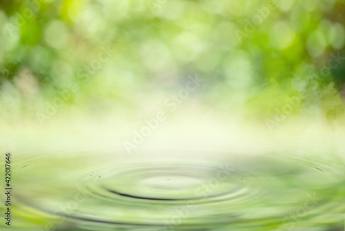 Drop falling in water with ripples with light green bokeh background.
