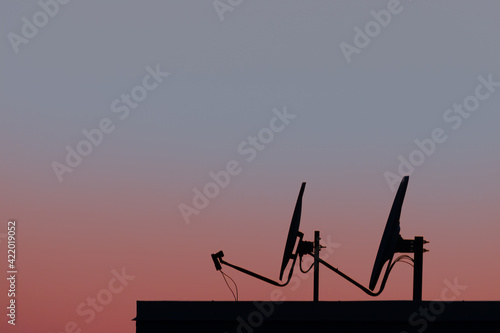 Isolated silhouette of satellite dishes. Sunset sky on the background with red and blue tones