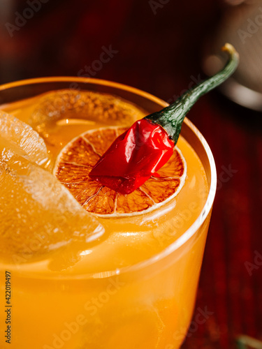 orange cocktail with a slice of orange and hot red pepper. On a wooden table