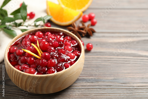 Fresh cranberry sauce with orange peel on wooden table, space for text