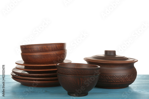 Different clay dishware on light blue wooden table against white background