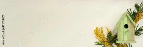 Stylish bird house and fresh mimosas on beige background. Space for text