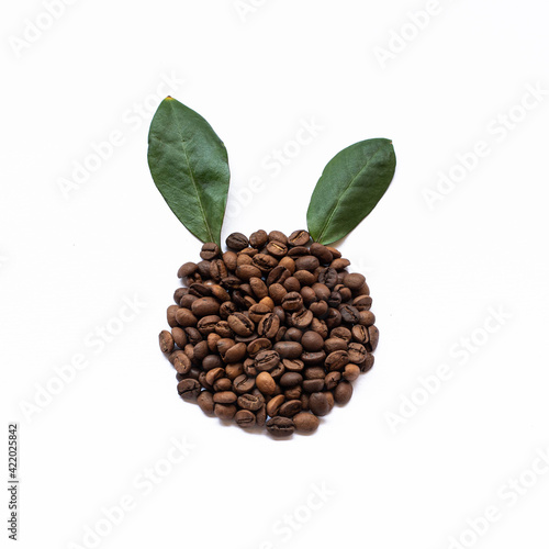 Coffee beans with green leafs in shape of rabbit on white background. Easter concept.
