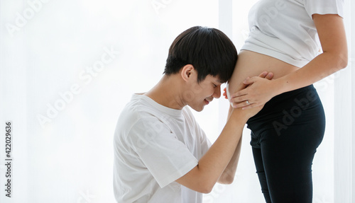 lovely family concept. Portrait of a young handsome Asian man and father wearing a white T-shirt sitting smiling happily while touching the belly of a pregnant woman