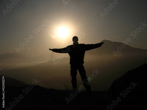 The silhouette of a man raised his hands against the background of the sunset