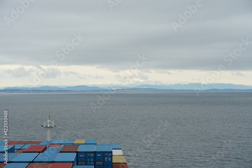 View form the container ship loaded with containers on the mountain covered with snow surrounding approach to Vancouver, British Columbia, from Pacific ocean.