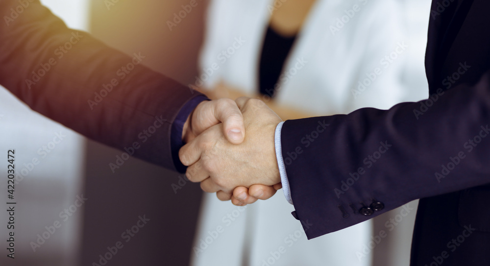 Unknown businesspeople are shaking their hands after signing a contract, while standing together in a sunny modern office, close-up. Business communication concept