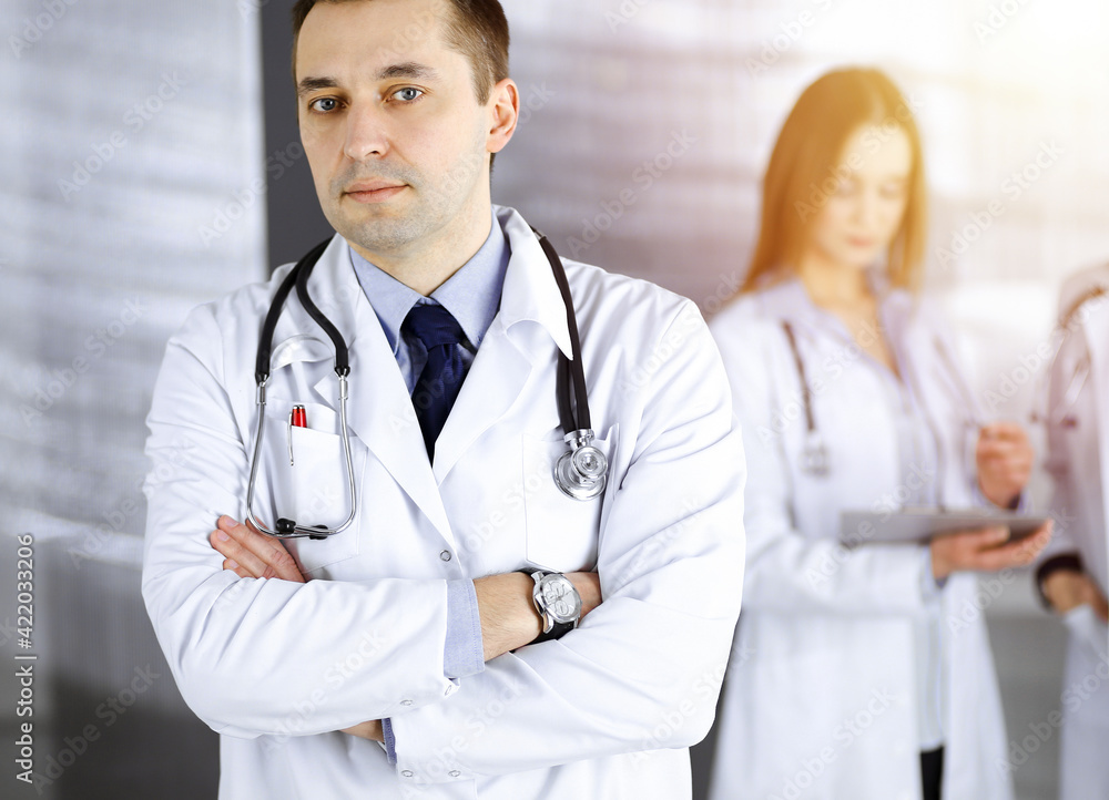 Professional doctor with a stethoscope is standing with crossed arms in a sunny clinic. Perfect medical service in hospital. Best medicine concept Professional doctor with a stethoscope is standing with crossed arms in a sunny clinic. Perfect medical service in hospital. Best medicine concept