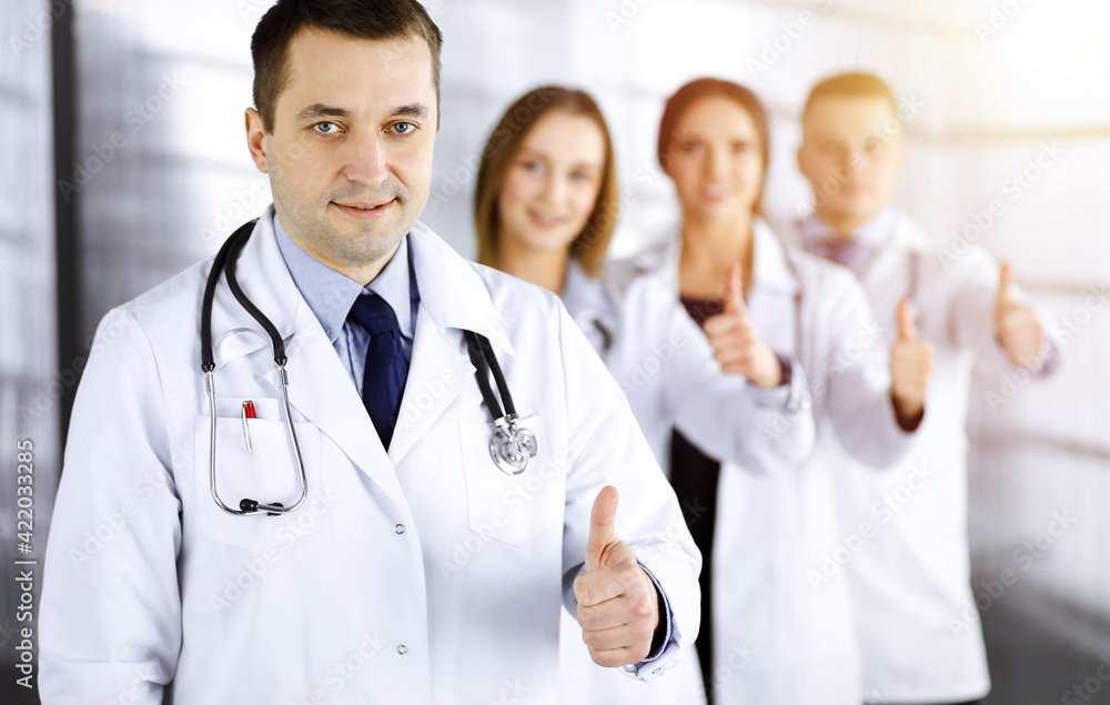 Group of professional doctors are standing as a team with thumbs up in a sunny hospital office, ready to help their patients. Best medical help, insurance in health care and medicine concept Group of professional doctors are standing as a team with thumbs up in a sunny hospital office, ready to help their patients. Best medical help, insurance in health care and medicine concept