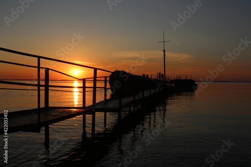 old pier bridge to the ship at sea at sunset with a mast