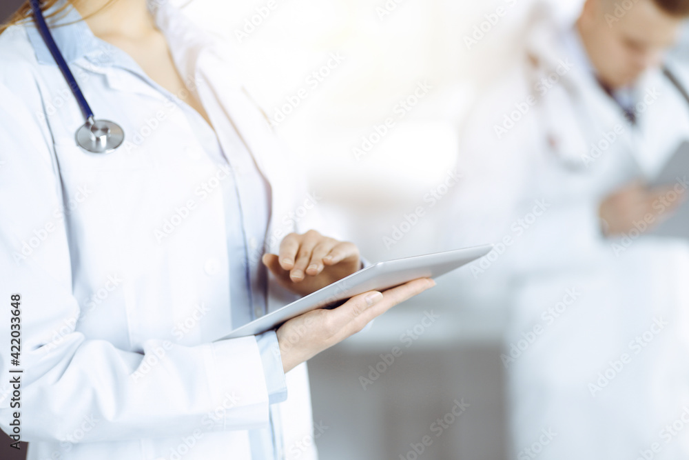 Unknown woman doctor is checking some data at computer tablet, close up. Young doctors at work in a sunny hospital. Perfect medicine and healthcare concept