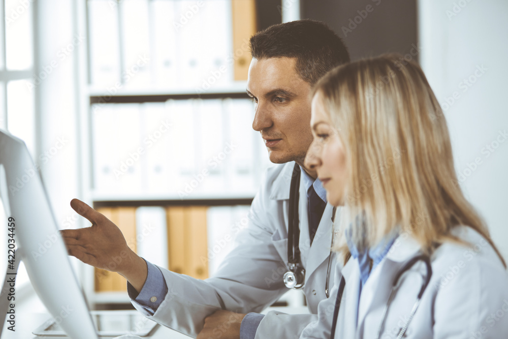 Two doctors colleagues discussing current disease therapy while sitting at working place in clinic. Team work in hospital. Medicine and healthcare concept Two doctors colleagues discussing current disease therapy while sitting at working place in clinic. Team work in hospital. Medicine and healthcare concept