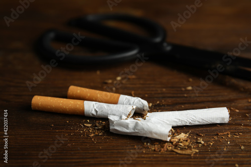Cut cigarettes and scissors on wooden table, closeup. Quitting smoking concept