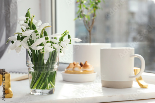 Beautiful snowdrops, cup of drink and dessert on white tray near window. Space for text