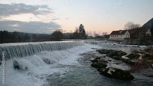 Sava river flowing over small manmade dam in Tacen, Slovenia. Wide river flowing over cascades and splashing on rocks. Left pan, wide angle, real time photo