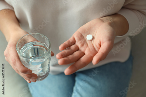 Fototapeta Young woman with abortion pill and glass of water on sofa, closeup