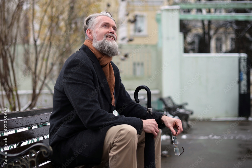 A gray-haired man sits on a park bench on a winter morning and enjoys the weather, looking at the sky