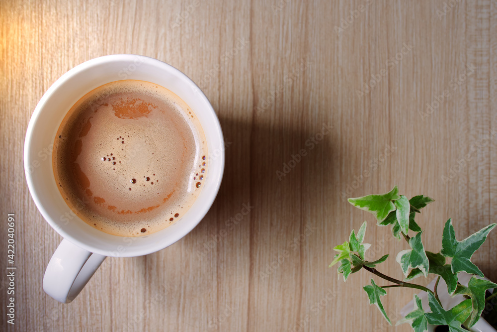 Obraz premium Top view of Coffee cup mixed milk froth or creamer and ivy plant on wooden table with copy space, Background image of drinks on wood texture in morning sunlight minimalist style and convey relaxation.