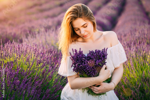 Young and happy blond woman and white dress enjoying spring in a lavender field at sunset