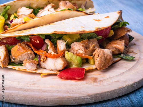 Mexican tacos with grilled chicken and vegetables on a wooden board close-up
