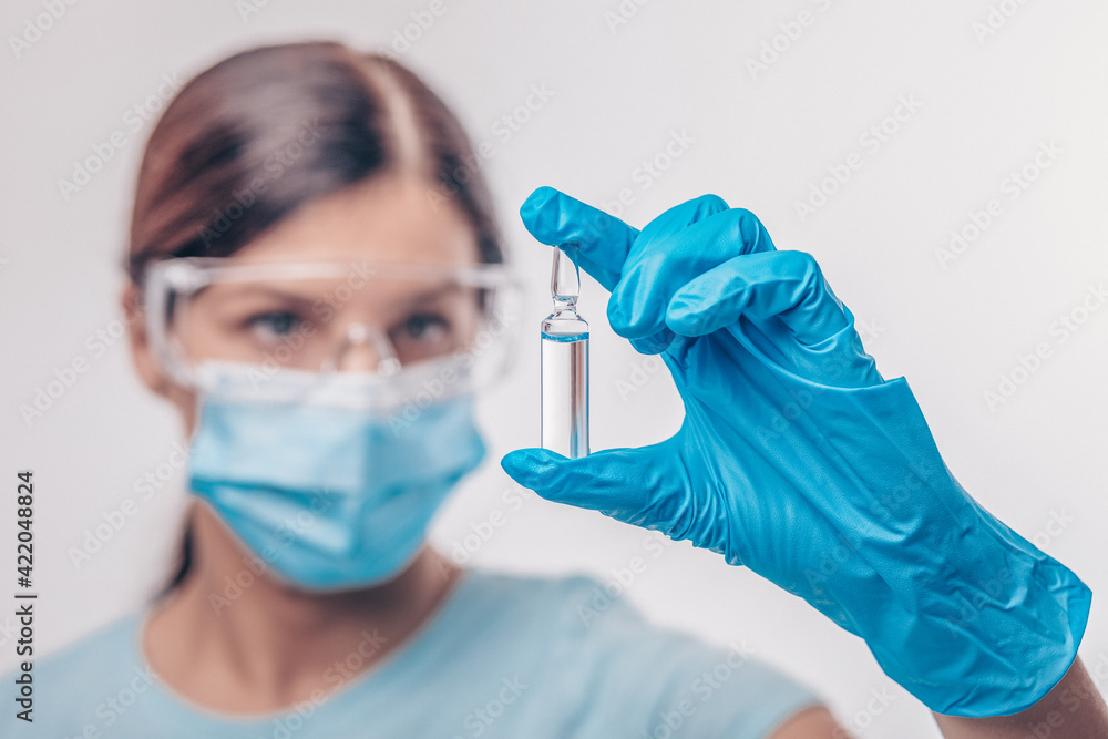Nurse in gloves and mask holding glass vial with injection liquid. Vaccination against influenza and coronavirus. Nurse in gloves and mask holding glass vial with injection liquid. Vaccination against influenza and coronavirus.