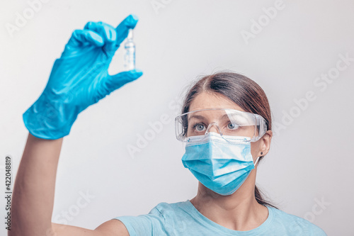 Nurse in protective gloves and mask holding glass vial with injection liquid. Vaccination against influenza and coronavirus.