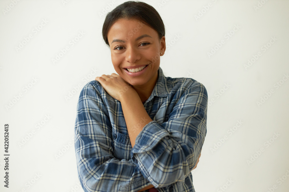 Charming young Afro American female wearing comfy shirt posing in studio hugging herself, expressing self love, looking at camera with broad happy smile. People and ethnic diversity concept Charming young Afro American female wearing comfy shirt posing in studio hugging herself, expressing self love, looking at camera with broad happy smile. People and ethnic diversity concept