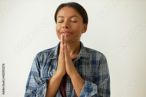 Prayer, positive vibrations and spirituality concept. Portrait of adorable grateful young dark skinned woman closing eyes with gratitude and bliss, keeping hands pressed together, being thankful