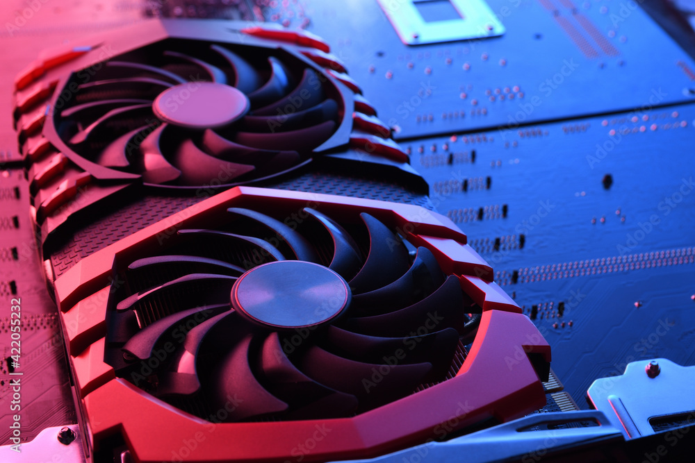 Fototapeta premium Computer game graphics card, videocard with two coolers on circuit board ,motherboard background. Close-up. With red-blue lighting