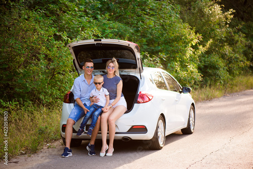 Family with a child sitting in the trunk of a car, preparing for a summer trip to the sea. © nagaets