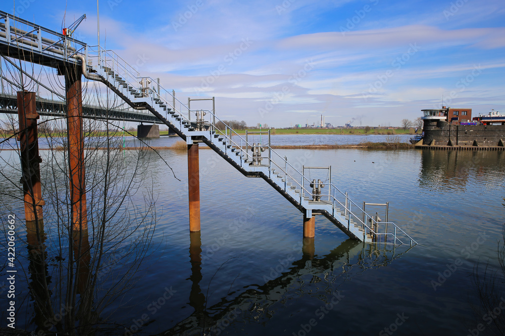 Krefeld (Ürdingen) - March 1. 2021: View on old dock steel stairway with river rhine and inland port factory building background (focus on stairway) Krefeld (Ürdingen) - March 1. 2021: View on old dock steel stairway with river rhine and inland port factory building background (focus on stairway)