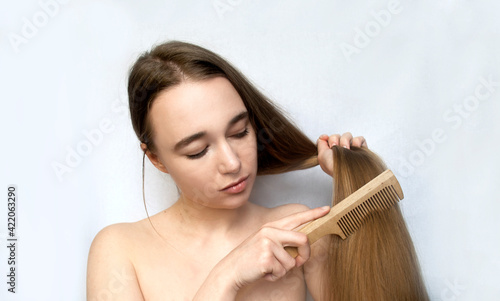 Young beautiful girl combing her long hair. Light background.