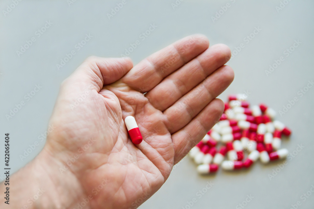 Red and white capsule on the palm of a hand on a background of the same capsules. Medicine. Pharmaceuticals. Bioactive additives. Vitamins. Illness. Disease.