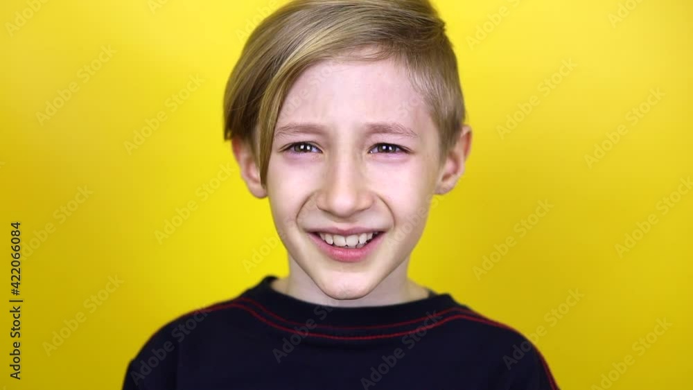 The boy is upset and begins to cry on camera. The child stands on a yellow background and shows emotions of sadness The boy is upset and begins to cry on camera. The child stands on a yellow background and shows emotions of sadness