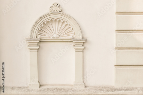 Decorative arch and semi vault above niche with classic pillars. Architectural stucco detail of old European buildingin Prague. Elegant masonry facade decor in beige color. No people, front view.