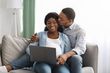 Loving pregnant black couple using laptop at home