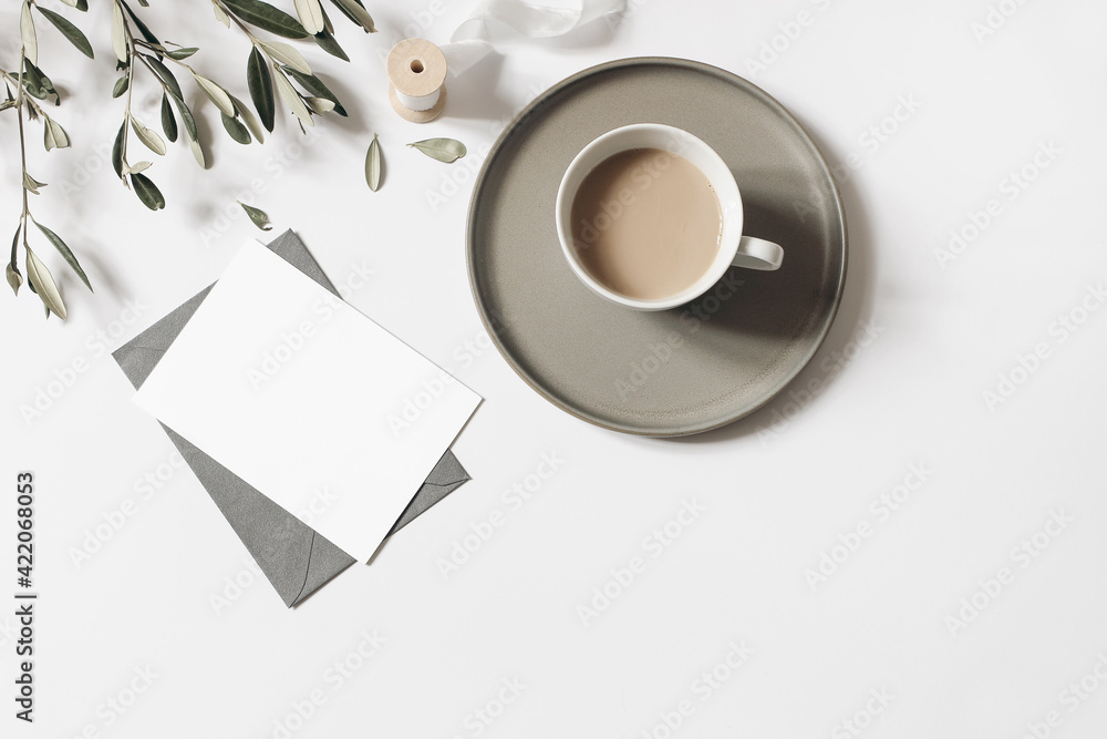 Blank greeting card, envelope mock-up. Cup of coffee, olive tree branches and silk ribbon isolated on white table background. Summer wedding, breakfast still life composition. Flat lay, top view. Blank greeting card, envelope mock-up. Cup of coffee, olive tree branches and silk ribbon isolated on white table background. Summer wedding, breakfast still life composition. Flat lay, top view.