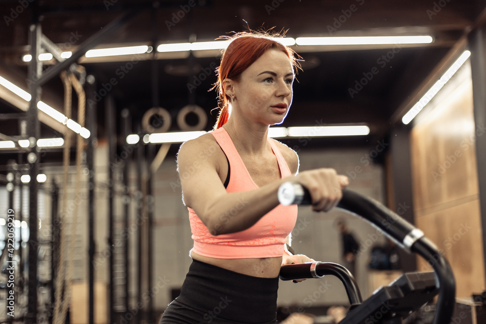 Fototapeta premium Redhead fit woman doing intense cardio training on exercise bike
