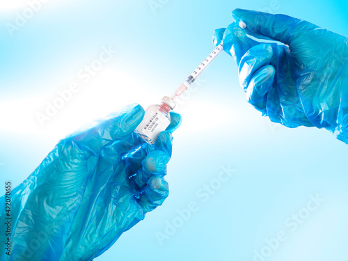 COVID-19 vaccine, researcher hands holds syringe and bottle of vaccine for coronavirus cure with clinic background. Concept of corona virus treatment