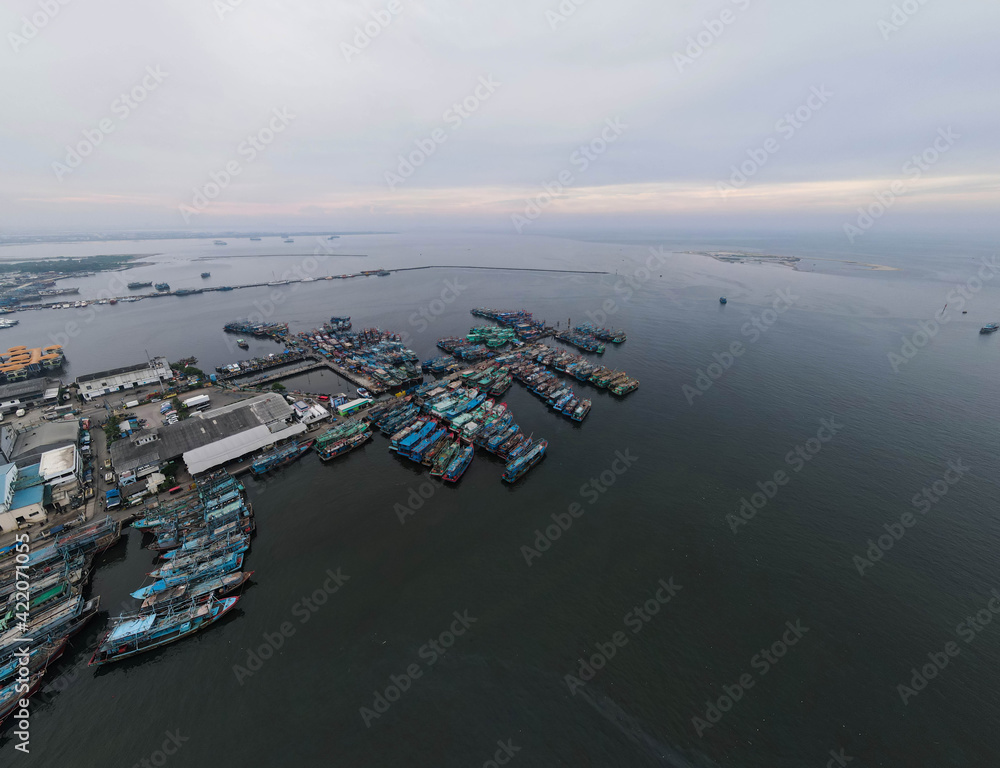 Aerial drone view of Muara Angke Beach with wooden boats leaning beside the pier. With noise cloud after rain. Jakarta, Indonesia. March 21, 2021