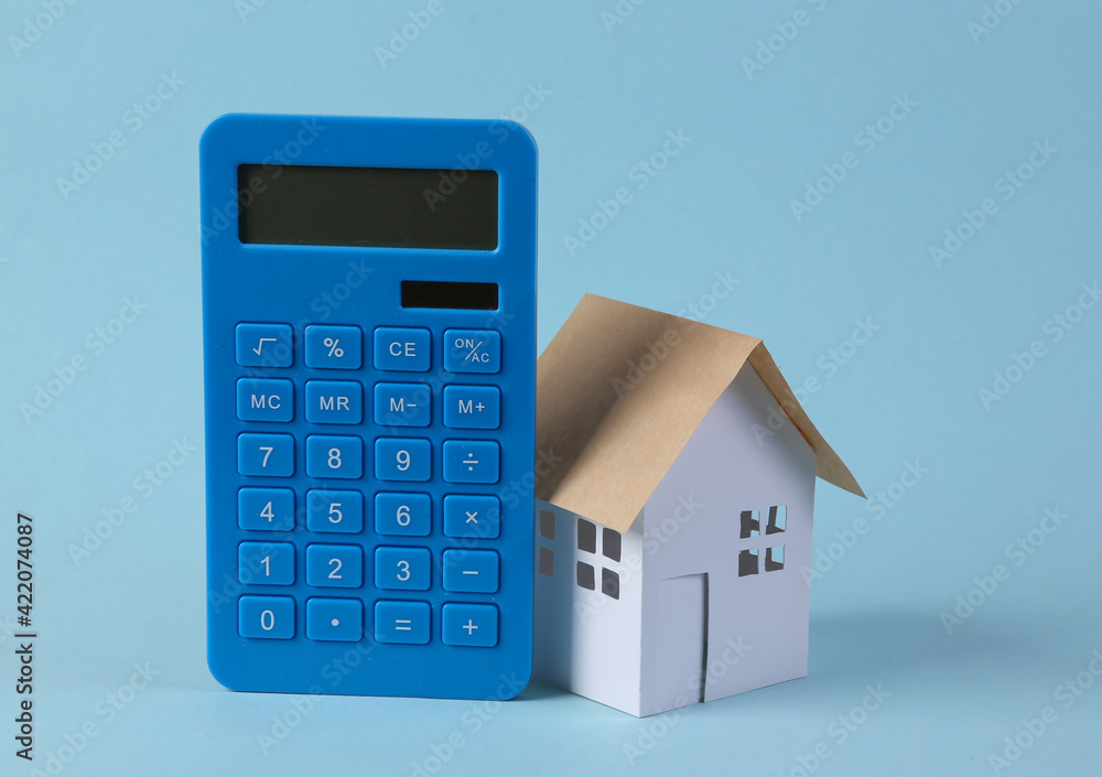 Calculator with small model house on blue background. Savings concept Calculator with small model house on blue background. Savings concept