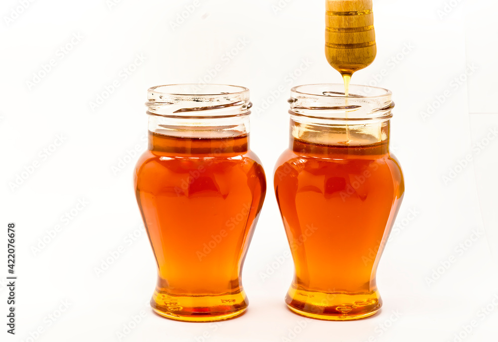 Honey dripping from wooden stick into glass jar, whte background Honey dripping from wooden stick into glass jar, whte background