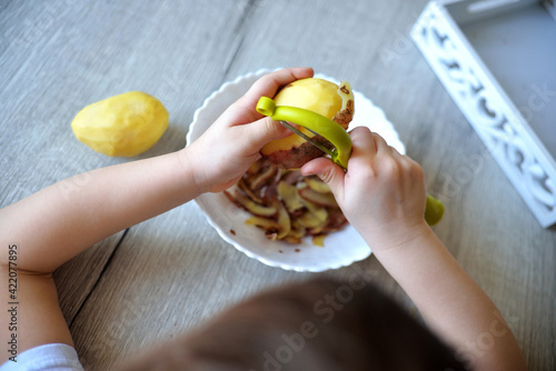 Children s hands peeling potatoes with montessori materials for a lesson from the practical life zone. peeler, potatoes, plate, tray.