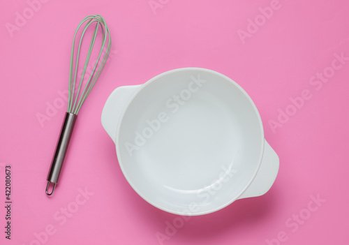 Cooking concept. Empty white bowl with whisk on pink studio background. Top view.