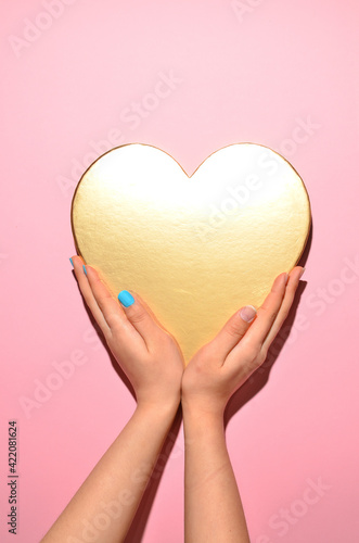 Stylish trendy female manicure. Beautiful young woman's hands with gold heart on pink background